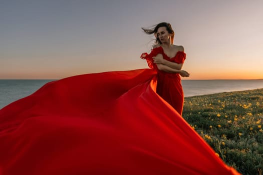 woman red dress standing grassy hillside. The sun is setting in the background, casting a warm glow over the scene. The woman is enjoying the beautiful view and the peaceful atmosphere