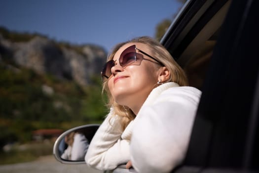 A blonde woman in a white sweater and jeans is driving. Happy woman sitting in the car