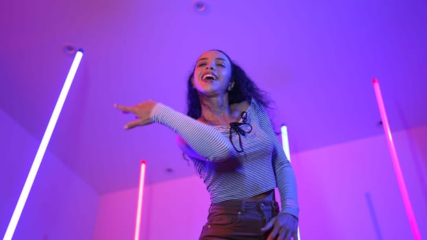 Low angle camera of hispanic dancer looking at camera and dancing to city pop music. Professional attractive hipster moving to hip hop song with purple led or neon light. Stylish cloth. Regalement.
