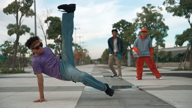 Attractive dancer perform break dance or freestyle dance in front of friend cheering at him. Professional handsome doing footstep while wear stylish cloth at park. Outdoor sport 2024. Sprightly.