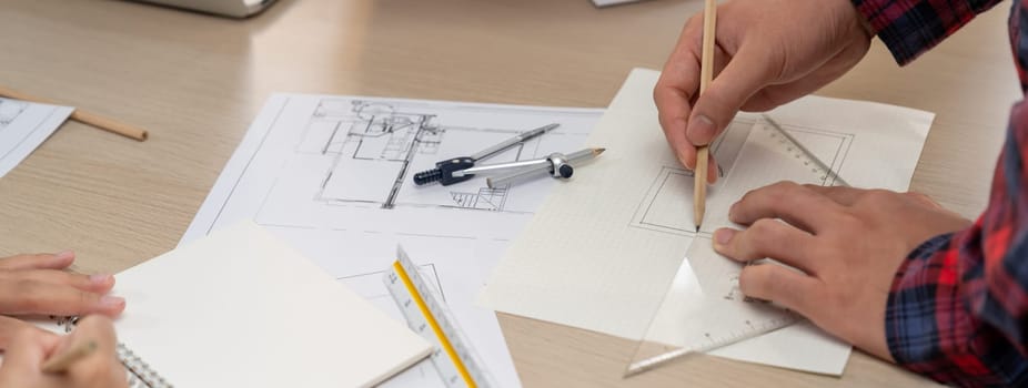 Professional architect hand drawing a blueprint by using ruler measuring length on table with architectural equipment and blue print scatter around at modern office. Closeup. Delineation.