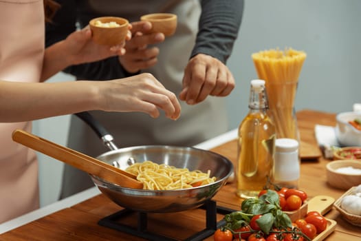 Close up of hand couple chef influencers cooking spaghetti mix ingredient taking to frying pan, putting seasoning and tasty sauce to make good flavor, Concept of presenting homemade food. Postulate.