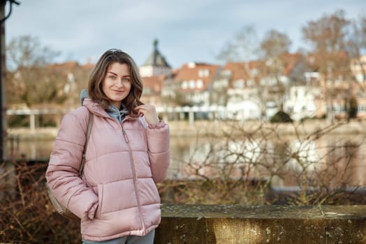 Young beautiful pretty tourist girl in warm hat and coat with backpack walking at cold autumn in Europe city enjoying her travel in Zurich Switzerland. Outdoor portrait of young tourist woman enjoying sightseeing