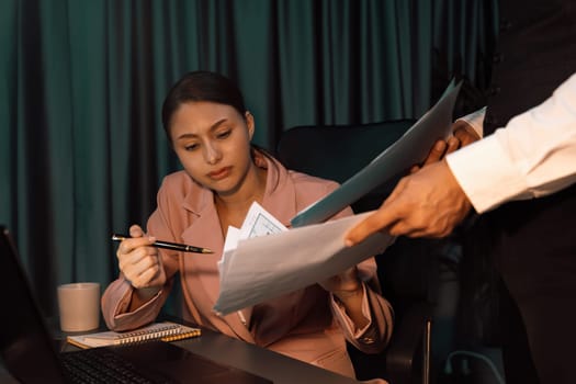 Focusing on serious face's woman with pink suit checking document for singing approved project with man's hand give business analysis market online graph paper at dark neon modern office. Postulate.