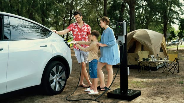 Outdoor adventure and family vacation camping in nature travel by eco friendly car for sustainable future. Lovely family recharge EV car with EV charging station in campsite. Perpetual