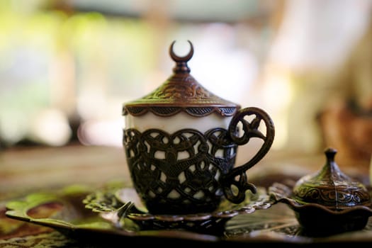A cup with a crescent moon on top sits on a tray. The cup is made of metal and has a white base. The scene is peaceful and serene