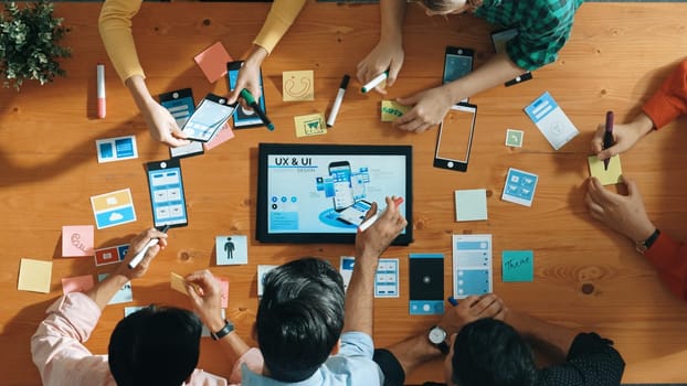 Top view of software developer team looking Ux Ui design for mobile phone interface from tablet while comparing and planning wireframe prototype designing together at creative workplace. Convocation.