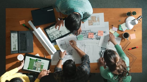 Top view of civil engineer team holding blueprint and standing at table with laptop, project plan and blueprint. Aerial view of skilled project manager planning and writing on sticky notes. Symposium.