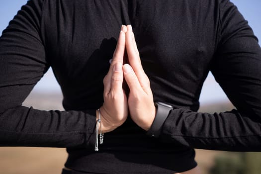 A person is praying with their hands clasped together. The person is wearing a black shirt and a wristwatch