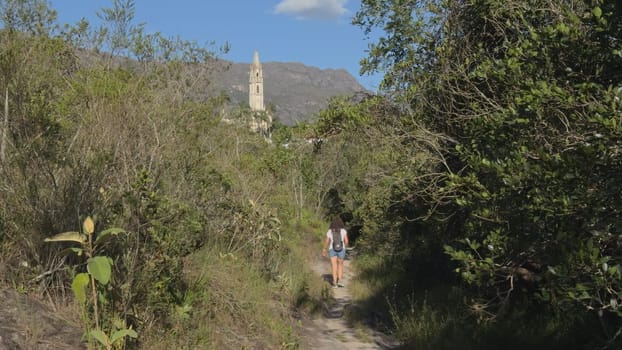 Hiker on trail with church tower background.