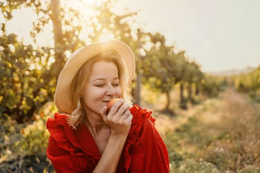 A woman in a red dress is eating an apple in a field. Concept of relaxation and enjoyment of nature