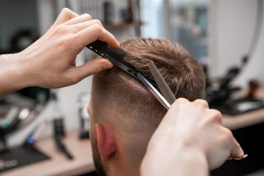 Barber shapes the mans hair with scissors and a comb at the barbershop