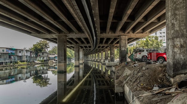 Bangkok, Thailand - Apr 20, 2024 - Perspective view of concrete pillars under Khlong Toei Expressway with Car parking and houses are old along the Khlong Phra Khanong. Copy space, Selective focus.