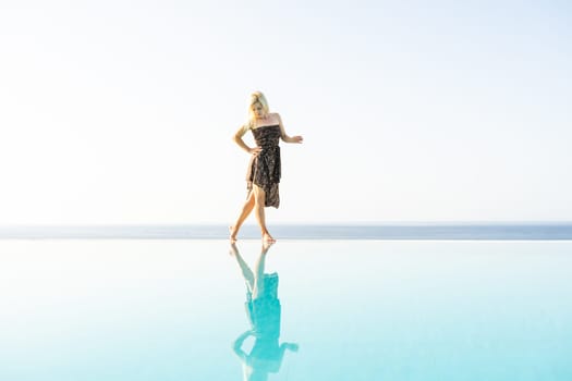 An attractive young woman stands near the pool with a panoramic view.