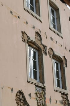 A close-up view of an old, deteriorating building facade with visible damage and exposed bricks around the windows.