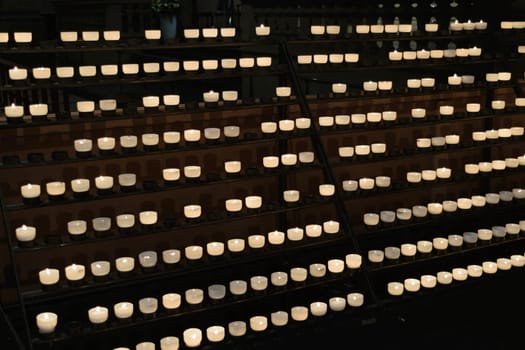 Rows of lit candles on a metal stand in a dimly lit setting.