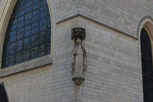 A stone statue of a religious figure on the exterior wall of a historic building with arched windows.