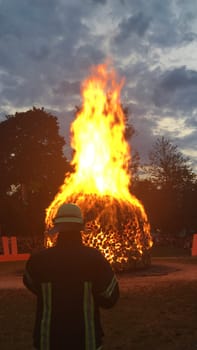 A large bonfire burning intensely with a person in protective clothing standing in front of it.