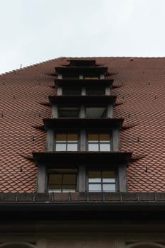 A close-up view of a building's roof with multiple windows and a unique architectural design. The roof is covered with reddish-brown tiles and features a series of small, stacked dormer windows.