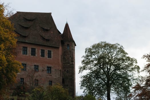 A historic brick castle with a tall tower and steep roofs, surrounded by trees.