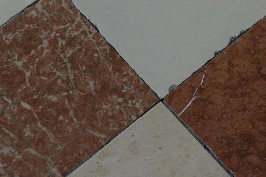 Close-up of a tiled floor with alternating brown and beige marble tiles arranged in a diamond pattern.