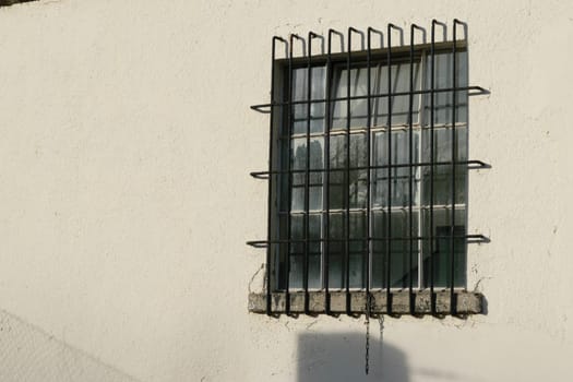 A small window with metal bars on a white concrete wall.