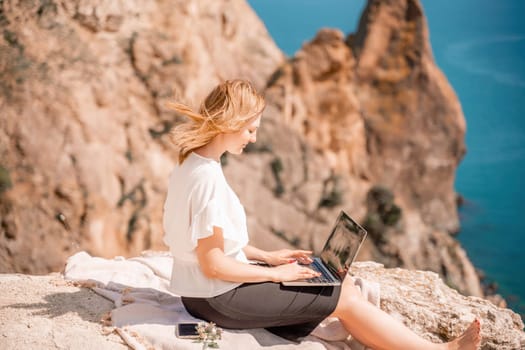 Freelance woman working on a laptop by the sea, typing away on the keyboard while enjoying the beautiful view, highlighting the idea of remote work