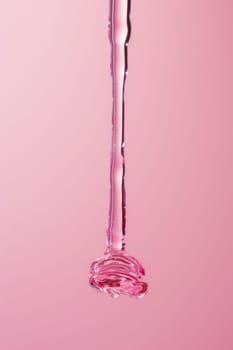 Pink liquid dripping from a glass bottle on a pink background for beauty and fashion makeup products concept