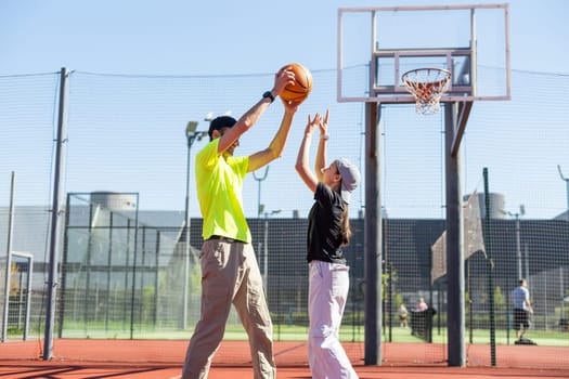 Father and teenage daughter playing basketball outside at court. High quality photo