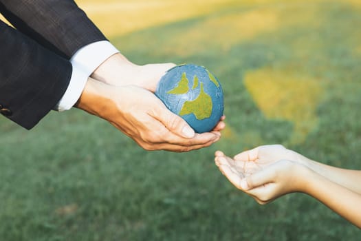 Businessman hand giving Earth globe to little boy as Earth day concept as corporate social responsible to contribute greener environmental protection for sustainable future generation. Gyre