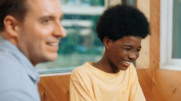 Smiling african boy sitting in circle while listening diverse friend sharing idea in group therapy with trust. Highschool student thinking and learning about mental health problem. Edification.