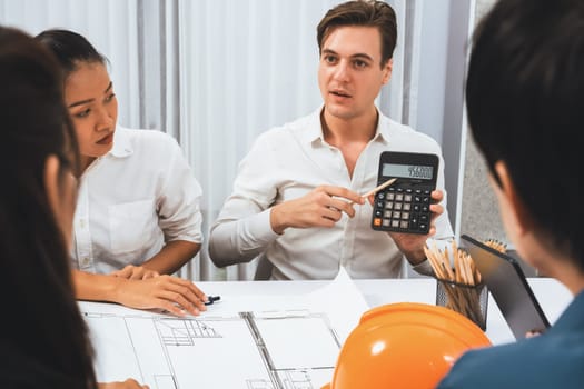 Diverse group of civil engineer and client working together on architectural project, building blueprint and calculate risk reduction for construction project at meeting table. Prudent