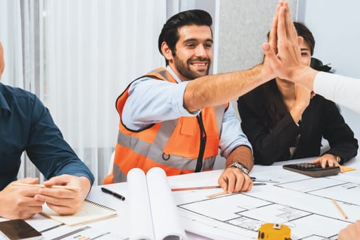 Diverse group of civil engineer and client celebrate and high five after make successful agreement on architectural project, reviewing construction plan and building blueprint at meeting table.Prudent