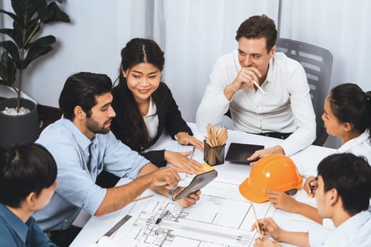 Diverse group of civil engineer and client working together on architectural project, reviewing construction plan and building blueprint at meeting table. Prudent