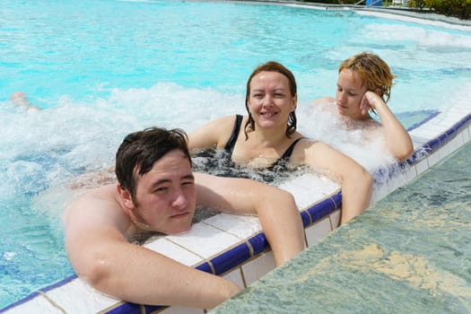 A group of people, possibly a family, are seen having a great time in a swimming pool, enjoying the water and relaxing in the hydromassage area.