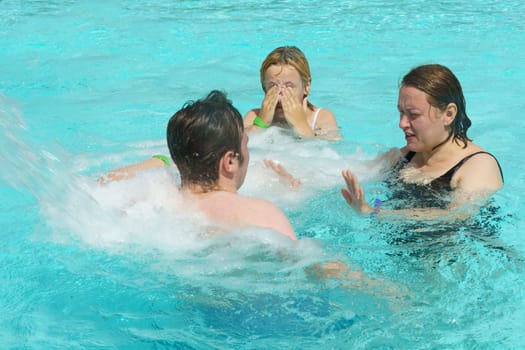 A group of individuals, likely a family, engage in playful activities in a swimming pool, enjoying the water and perhaps utilizing the hydromassage feature for relaxation.