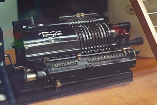 Warsaw, Poland - August 8, 2023: A vintage Triumphator CN adding machine sits on a wooden desk in a well-lit room. The machines intricate design and mechanical components are clearly visible, evoking a sense of nostalgia and historical significance.