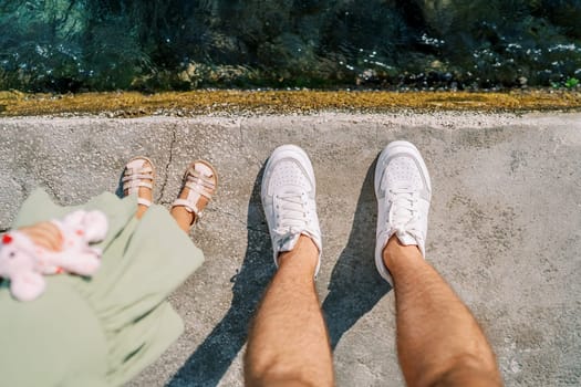 Legs of a dad and a little girl standing on the seashore. Top view. Cropped. Faceless. High quality photo