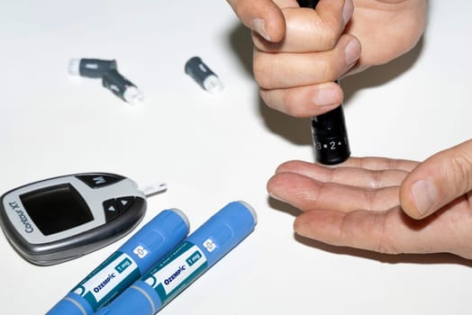 Diabetic man measuring blood sugar level. Blood test for diabetes and injection pen with Ozempic insulin. Denmark - February 10, 2024