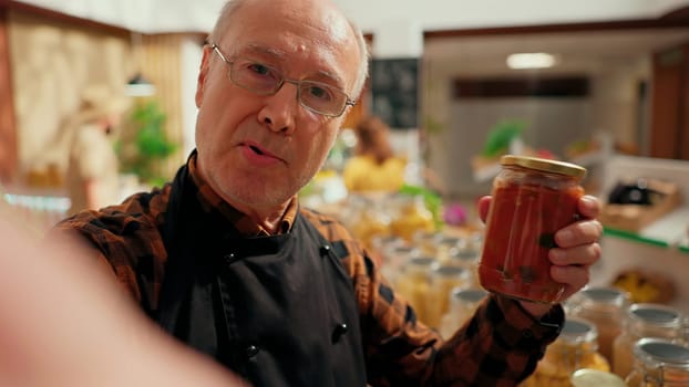 Local neighborhood supermarket elderly owner films promotional vlog showing high quality organic vegan products. Entrepreneur doing marketing video presenting fresh produce in his zero waste store