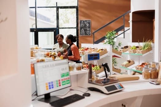 In eco friendly store, vendor with an apron assisting customer in selecting fresh bulk products with plastic free packaging. Black women standing in bio food shop, talking about sustainable lifestyle.