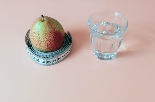 Concept of healthy lifestyle and proper nutrition. A glass of water and a pear with a measuring tape.