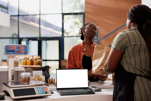 Blank white screen displayed on laptop while black woman with glasses receives her zero waste package. Isolated device with copy space for advertising or promotion of eco friendly bio food store.