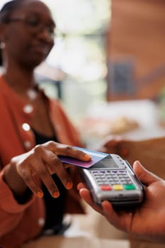 An African American individual making a contactless payment with a debit card to purchase fresh organic produce at a nearby market. Black woman paying with card at checkout counter.