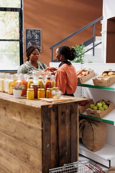 At eco-friendly store, african american farmer delivers crates of fresh produce to woman wearing spectacles. An apron wearing vendor taking boxes of freshly harvested fruits from female merchant.