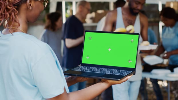 Detailed view of african american female volunteer holding laptop with isolated copyspace display for customization. Black lady holds minicomputer with green screen chromakey template in her hands.