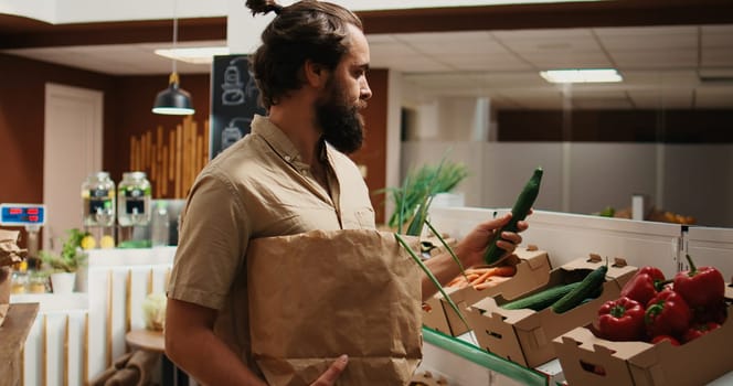 Man in zero waste shop buying vegetables, checking products before making purchase decision to ensure they are pesticides free. Vegan client verifying food in local store is organic, smelling it