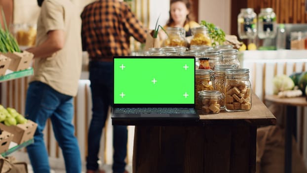 Chroma key laptop with copy space used as commercial sign in sustainable local shop. Promotional ad on green screen device in food store with products in reusable glass jar package