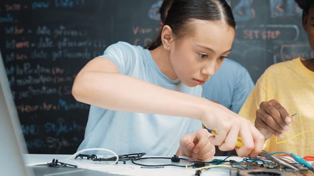 Happy highschool student using electronic tool fixing board while caucasian teacher help preparing car robot at STEM technology class. attractive girl working by using wire and mainboard. Edification.