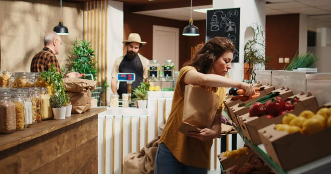 Tracking shot of woman in zero waste supermarket using nonpolluting paper bag while shopping for vegetables. Client in local shop using no single use plastics policy to save planet